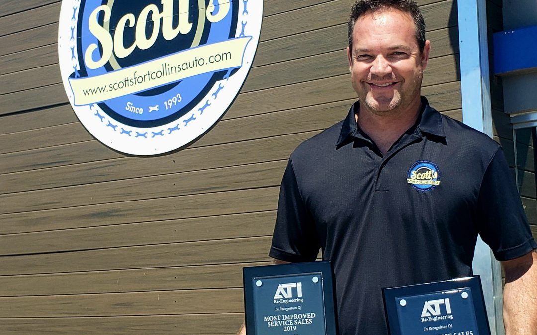 Scott Milan smiling outside a Scott's Automotive building while proudly holding two ATI awards for "Most Improved Service Sales 2019" and "Best Service Sales 2019."