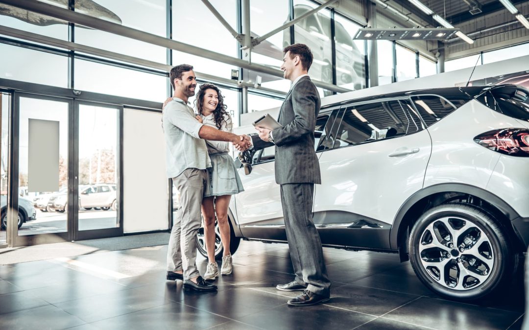 A smiling young couple shaking hands with a professional sales representative or service advisor in a spacious, modern automotive showroom next to a white SUV, highlighting pre-purchase inspections and friendly customer care services at Scott's Auto.