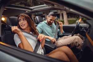 A young couple that is buckling their seatbelts before leaving in their vehicle.