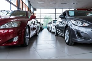 A view of cars inside a dealership. You can see half of one of the cars (red) on the left side of the photo and a charcoal one on the right side of the photo. 
