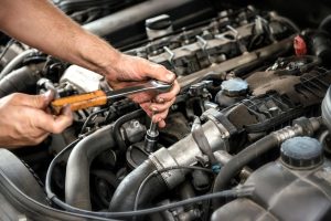 Mechanic using a wrench and socket on the engine of a motor car during a service or repair in an automotive workshop, close up of his hands