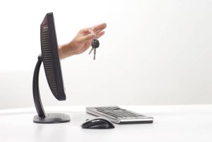 A view of a desktop computer , keyboard and mouse. There is a person's hand coming out of the screen holding new car keys.