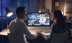 A view of a couple in the evening that are looking at a car site online. 
