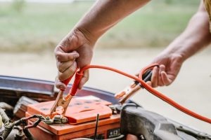 A close-up view of a person putting jumper cables on their car battery to get it charged.