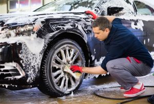 A driver cleaning his black car by hand.