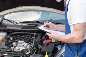 A car professional that is making notes on a clipboard as he is working on it.