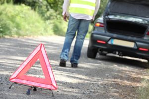 A man walking back to his car after setting out a hazard triangle behind his car.