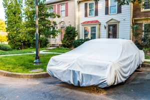 Image of a car with a cover over it as it is parked outside a house in a driveway.