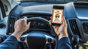 A view from the driver's seat of the steering wheel. The driver is holding up a phone that says 