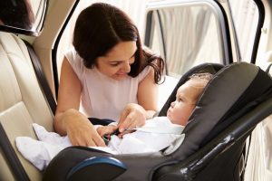 A woman is fastening her small baby into a car seat before driving her car.