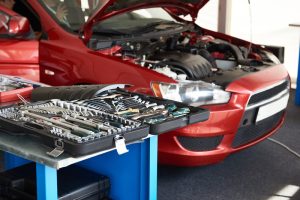 An image of a car with the front hood up and a bunch of car tools in a body shop.