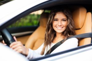A brunette woman in a car smiling out the window at the camera.