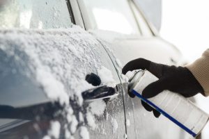 A close-up view of a de-icer solution being used on a lock and door handle of a car. 