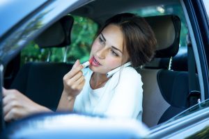 Woman that is talking on the phone and putting on lipstick while she drives