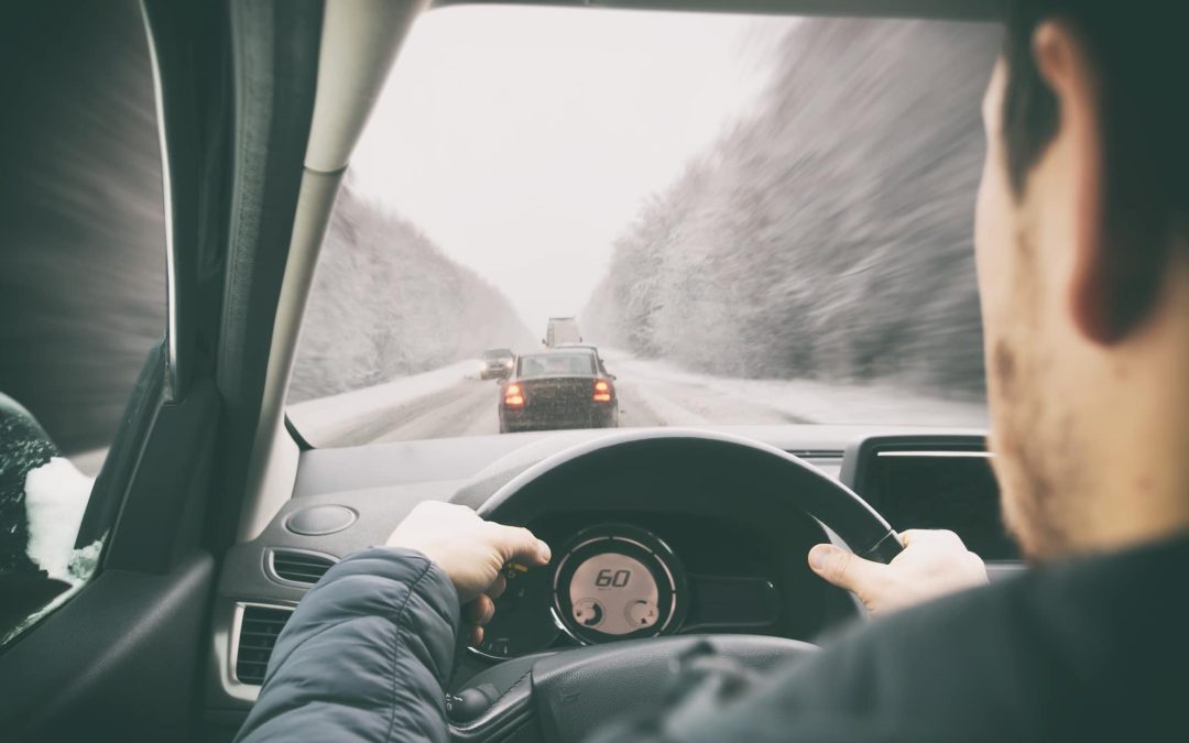 An over-the-shoulder view of a driver navigating a vehicle down a winter highway behind traffic on a snowy day, highlighting the importance of responsive braking systems, winter tire safety, and seasonal vehicle maintenance at Scott's Auto.