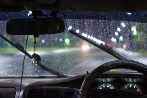A view of what a driver would see inside a car while it is raining outside and the window wipers are going back and forth.
