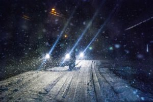 Various cars that are driving towards the camera with headlights on in the snow.