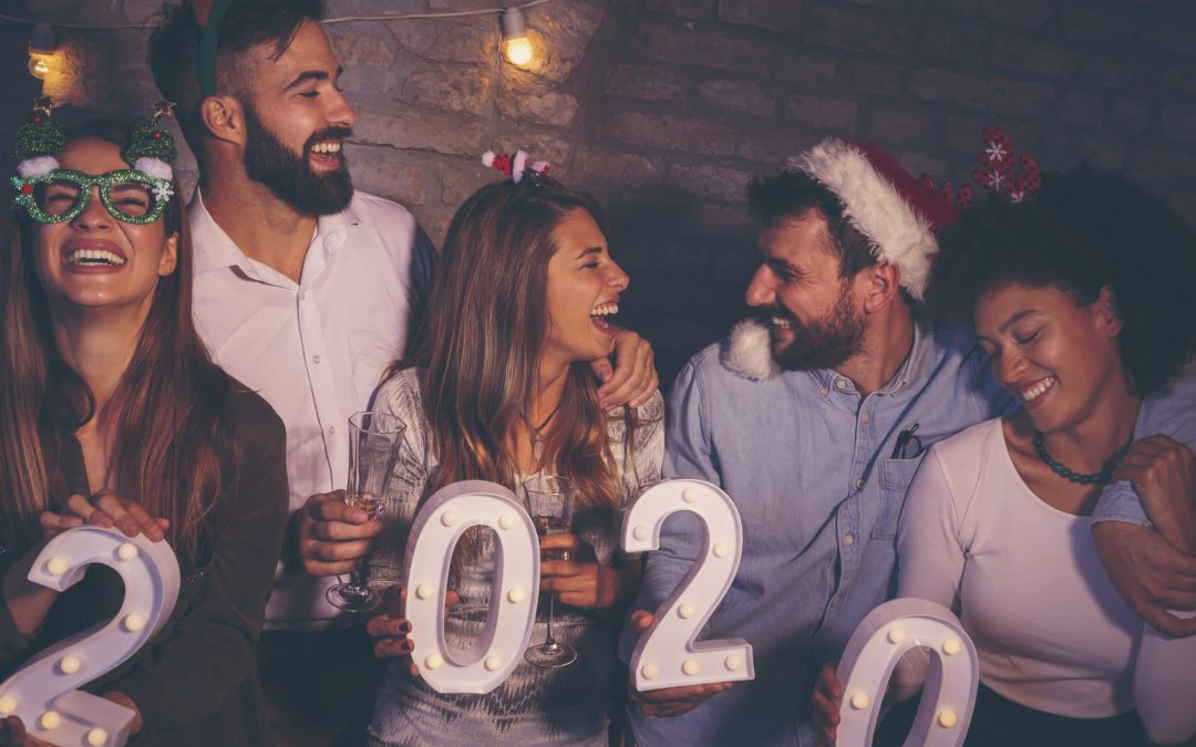 A joyful group of friends laughing and celebrating together at a holiday party while holding up illuminated "2020" marquee numbers, reminding drivers to stay safe during holiday celebrations with reliable designated drivers and expert vehicle maintenance services from Scott's Auto.
