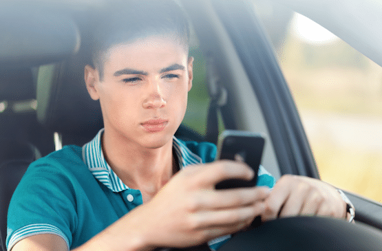 A close-up view of a young driver looking down at a smartphone while behind the wheel of a vehicle, emphasizing the crucial need for driver focus, distraction prevention, and advanced vehicle safety feature inspections at Scott's Auto.