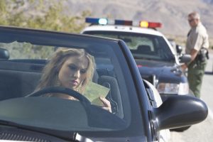 A woman who has just gotten a ticket for breaking a traffic law. You can see a police officer returning to his car in the background.