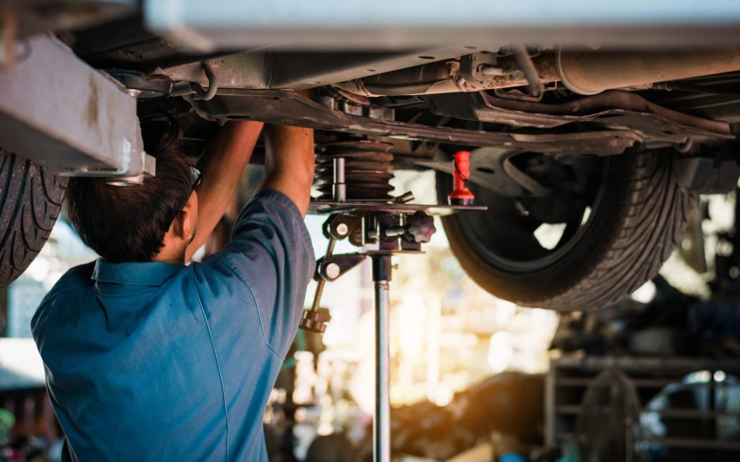 A professional mechanic working underneath a vehicle raised on a hydraulic lift in a repair shop, highlighting expert suspension repair, undercarriage diagnostics, and routine tune-up services available at Scott's Auto.