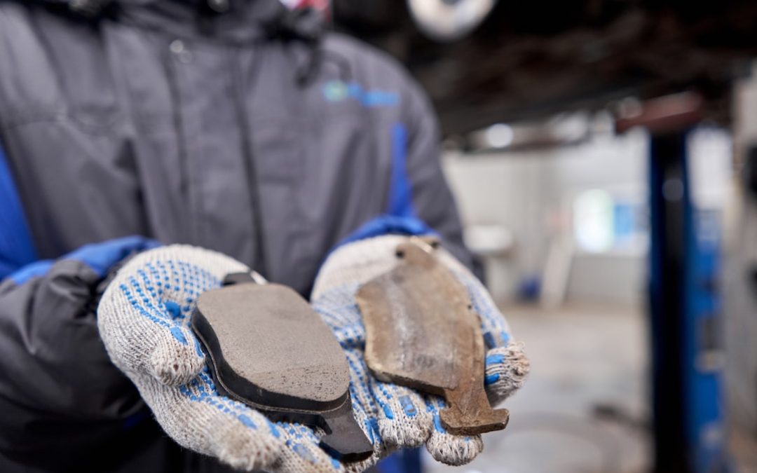 The mechanic holds the old and new brake pads in his hand. Change the old to new brake disc on car in a garage. Auto repair concept.