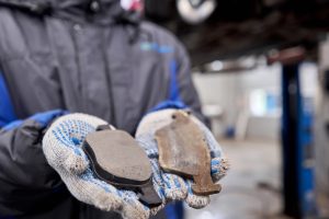 The mechanic holds the old and new brake pads in his hand. Change the old to new brake disc on car in a garage. Auto repair concept.