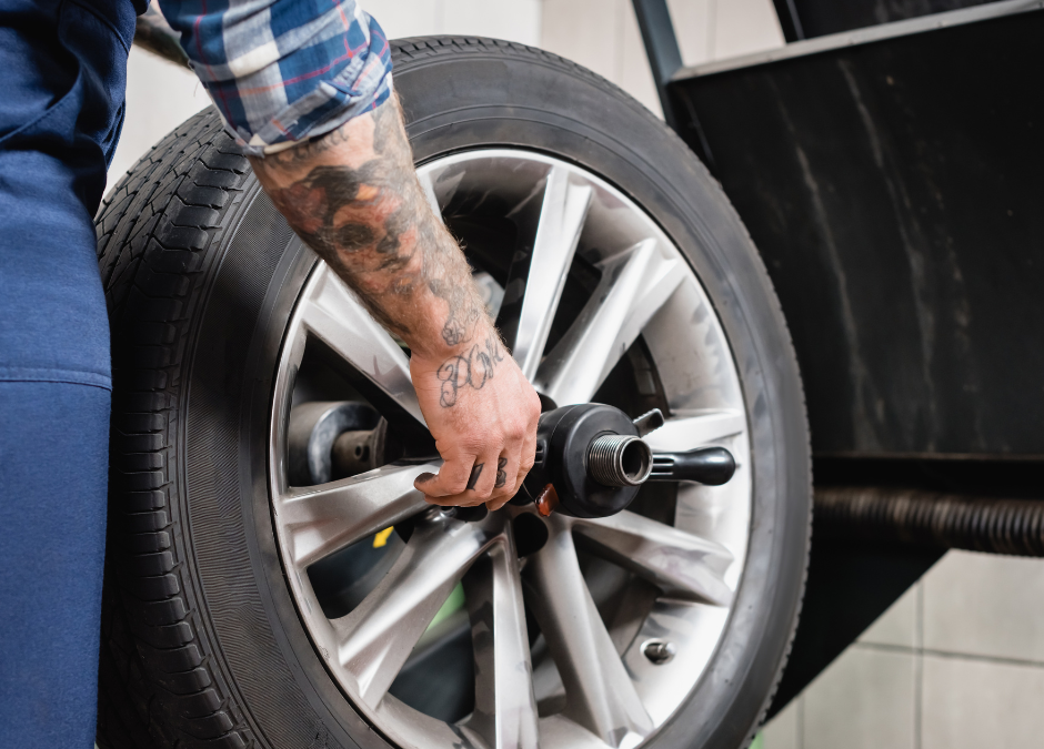 A mechanic placing a car tire back onto a vehicle at an auto shop, ensuring proper installation for safety and performance.