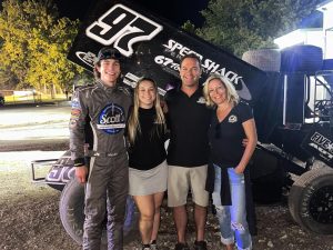 The Milan family alongside a #97 racing car, associated with Scott's Automotive racing sponsorships or events.